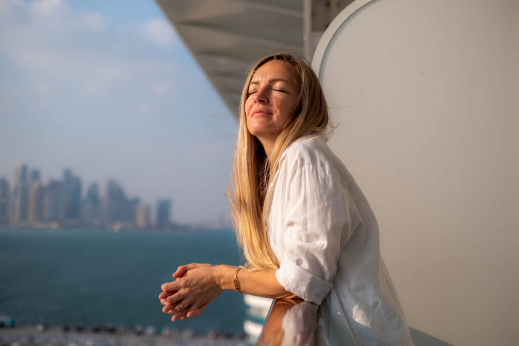 a woman on the terrace of a cruise ship enjoys the sun shining on her