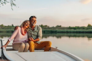Senior couple holding hands and laughing while enjoying a romantic boat trip on the lake at sunset